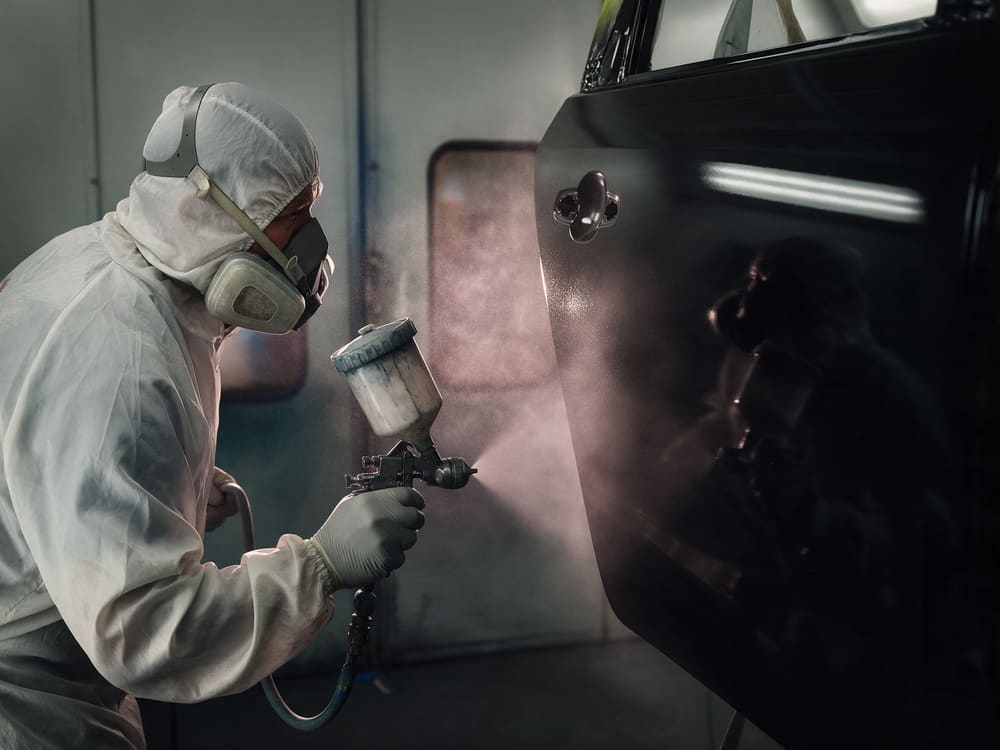 Painter spraying a black car door in a downdraft paint booth